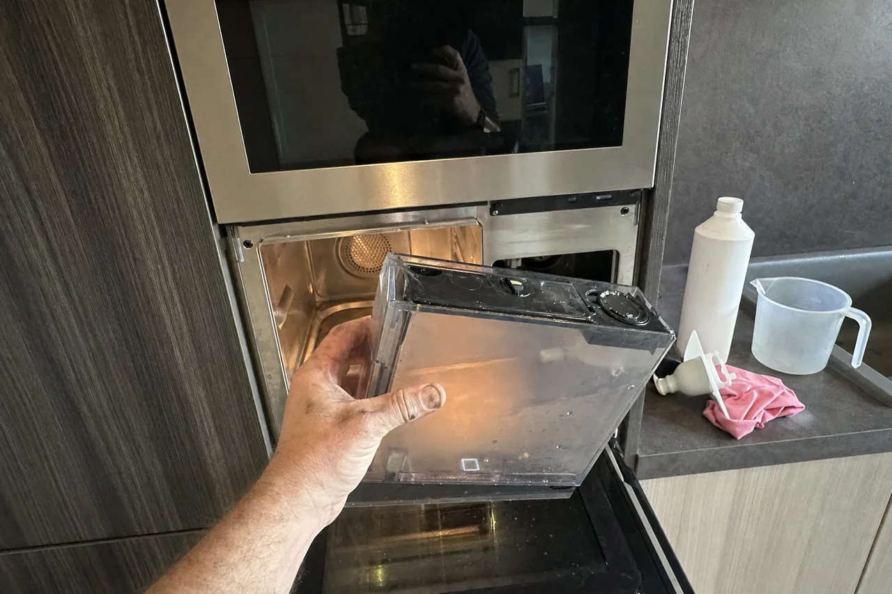 Built-in oven column in a timber cabinet run with the lower door standing open and the upper appliance dark above it